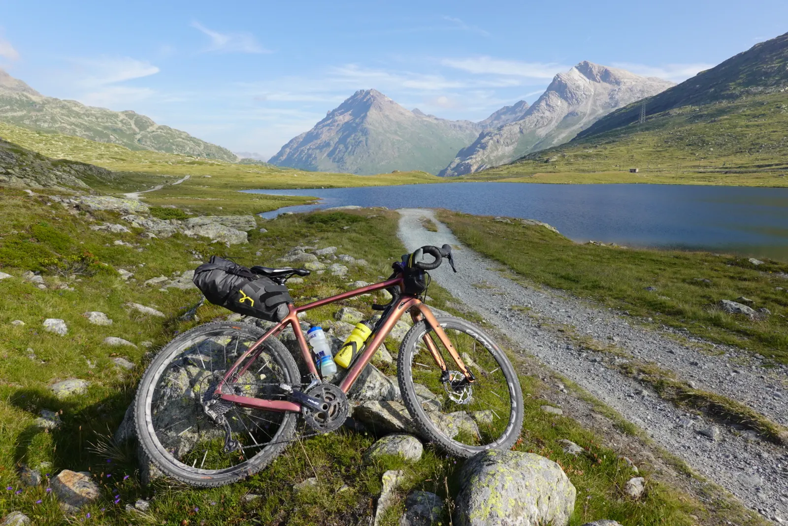 The loaded gravel bike beside a gravel path along a mountain lake, high peaks behind