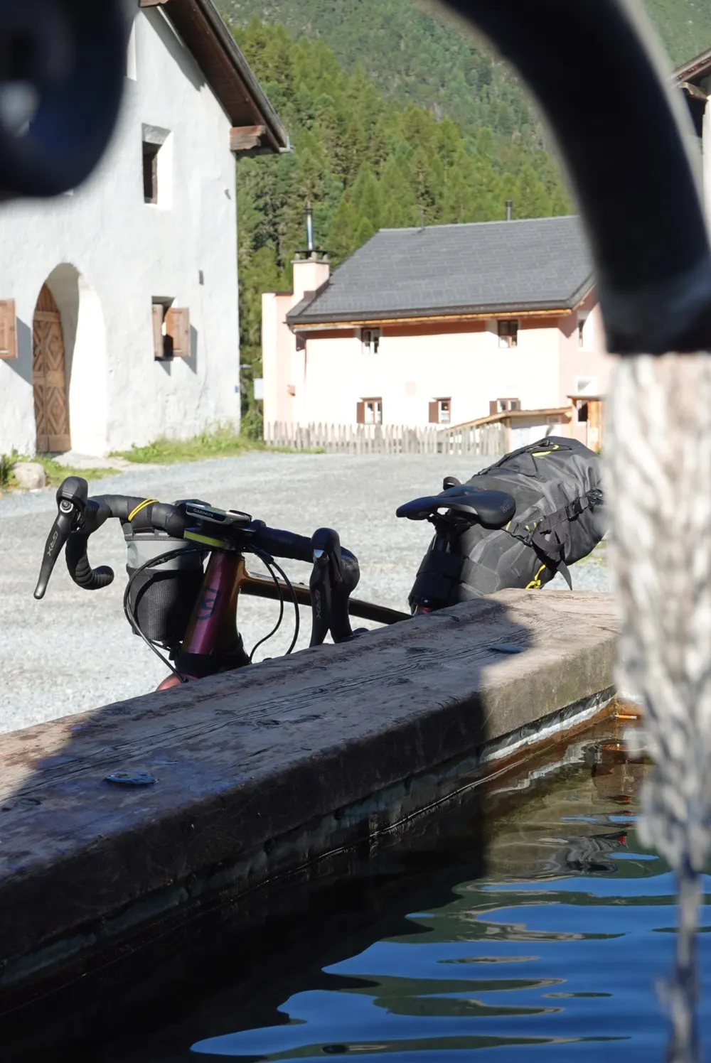 The gravel bike leaning against a wooden fountain in front of old houses in a mountain village