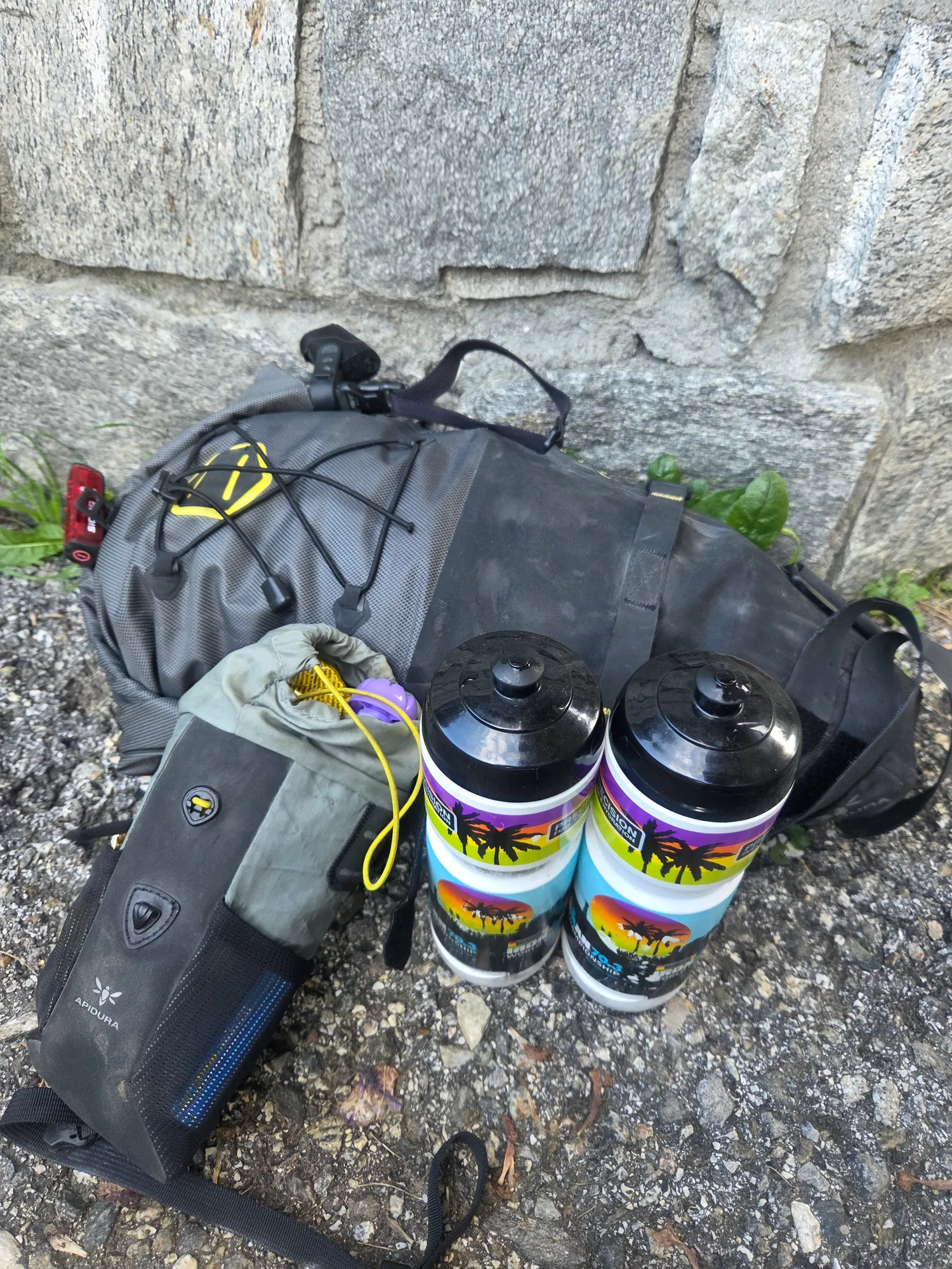 Packed bikepacking bags and two water bottles against a stone wall