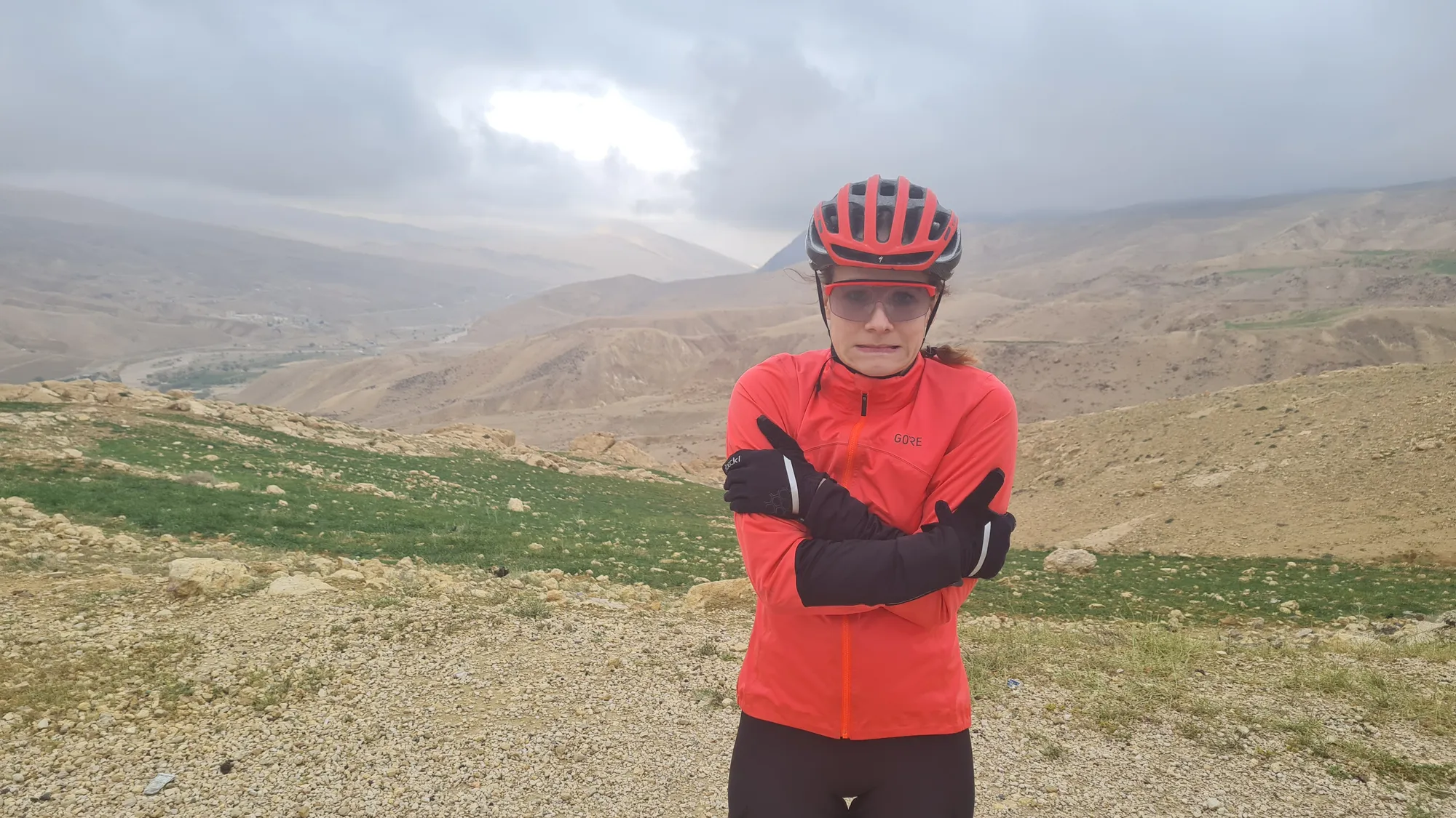 In a red jacket, arms crossed, under a grey sky
