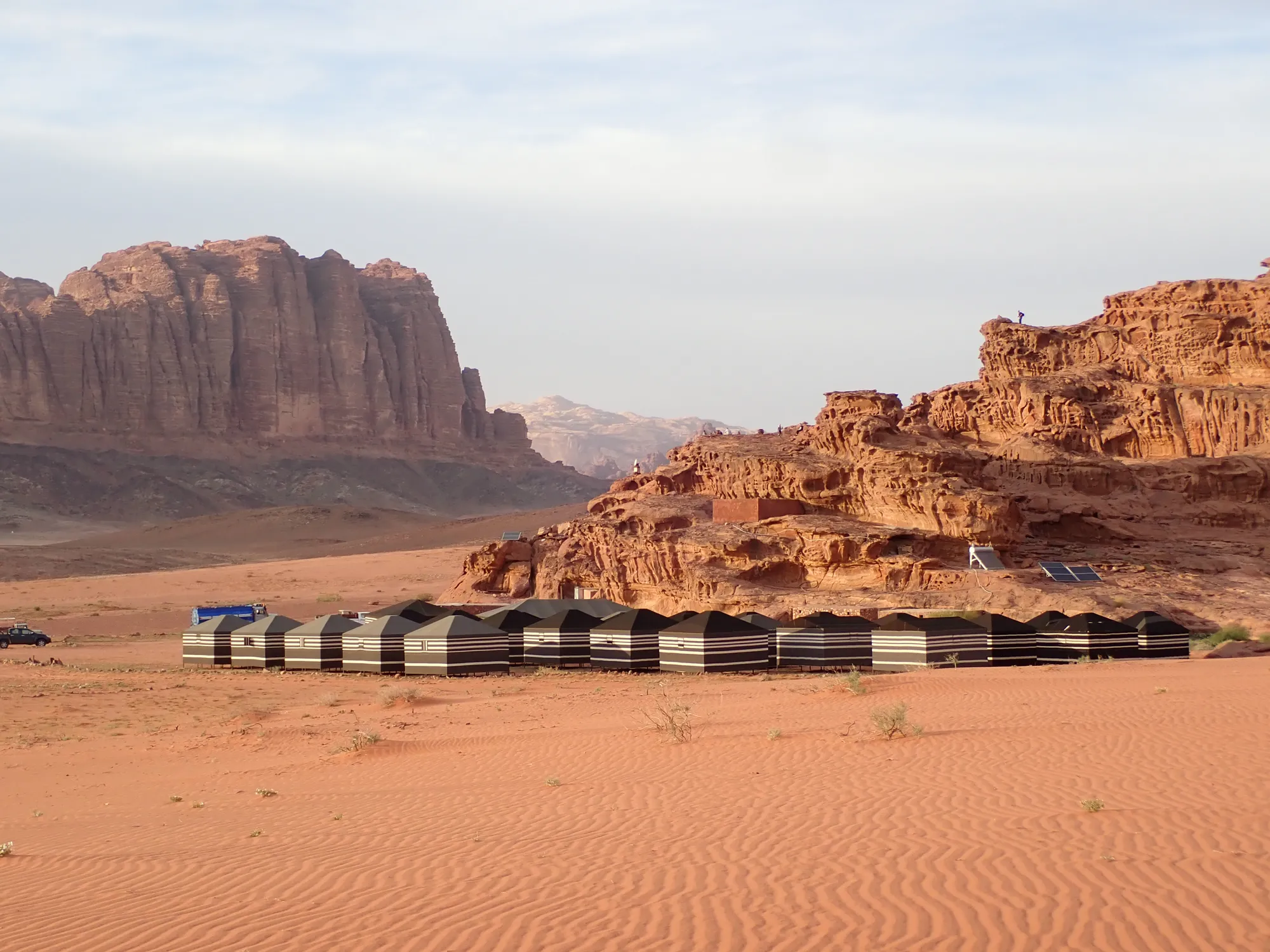 Desert camp in red sand in front of rock walls