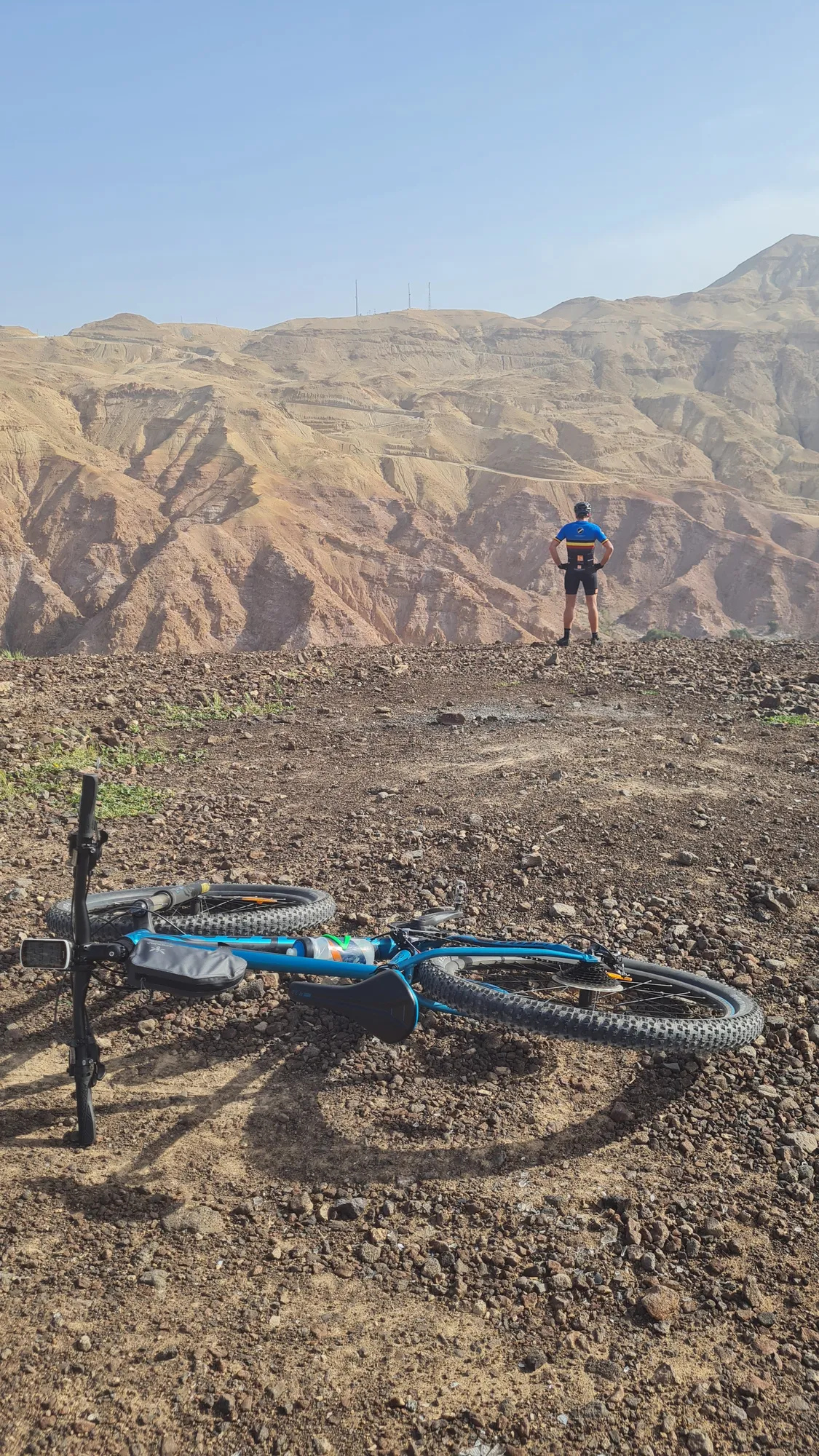 Mountain bike on the ground, a rider from the group in front of colourful, rugged mountains