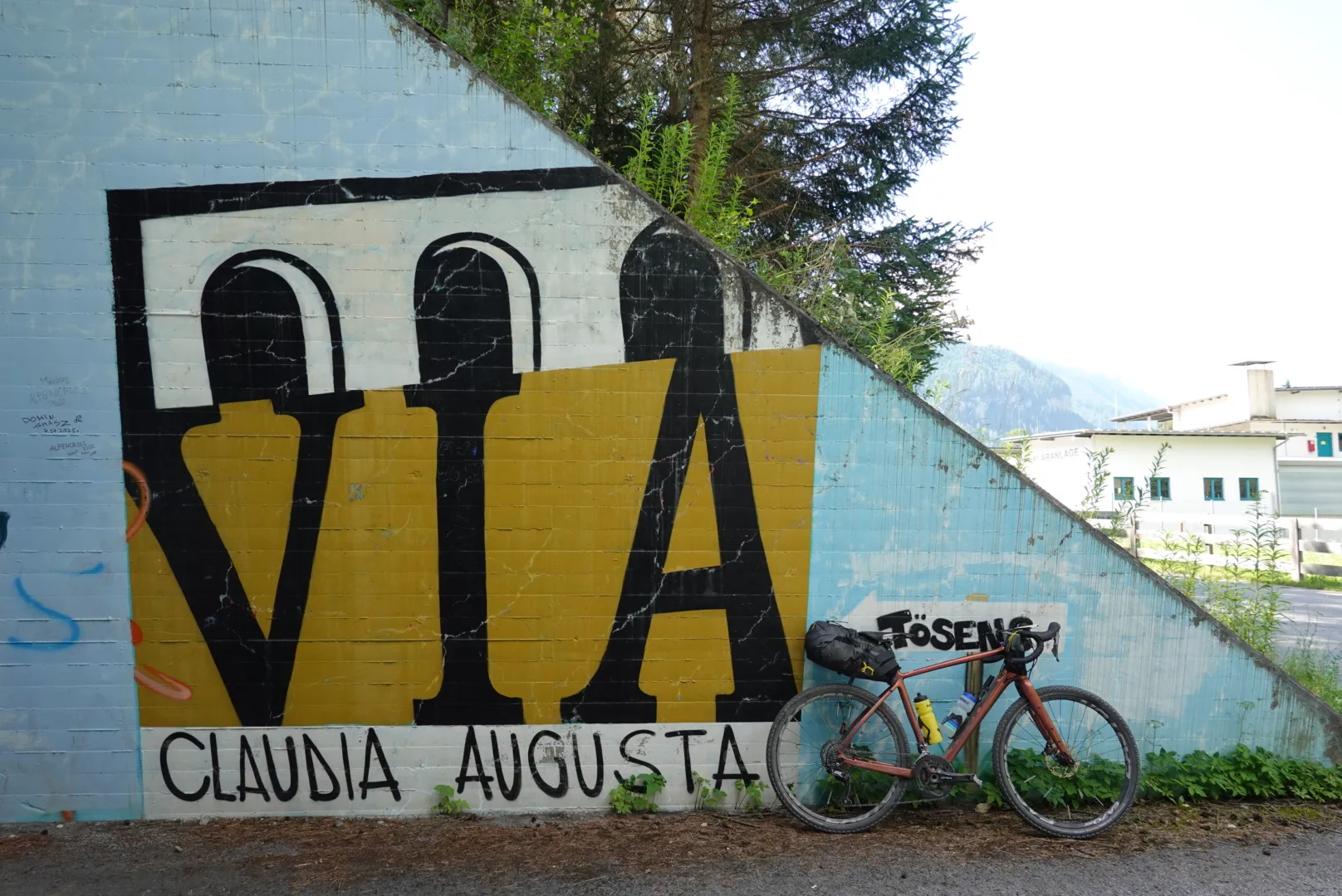 Loaded gravel bike in front of a "Via Claudia Augusta" mural
