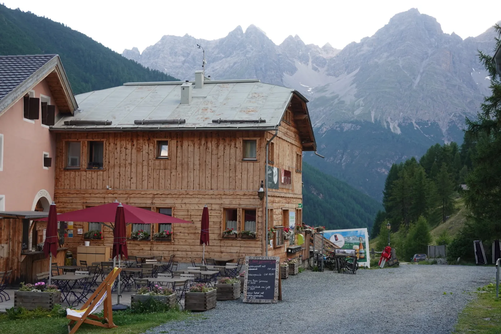 The guesthouse in S-charl with a wooden façade and parasols in front of rocky mountains