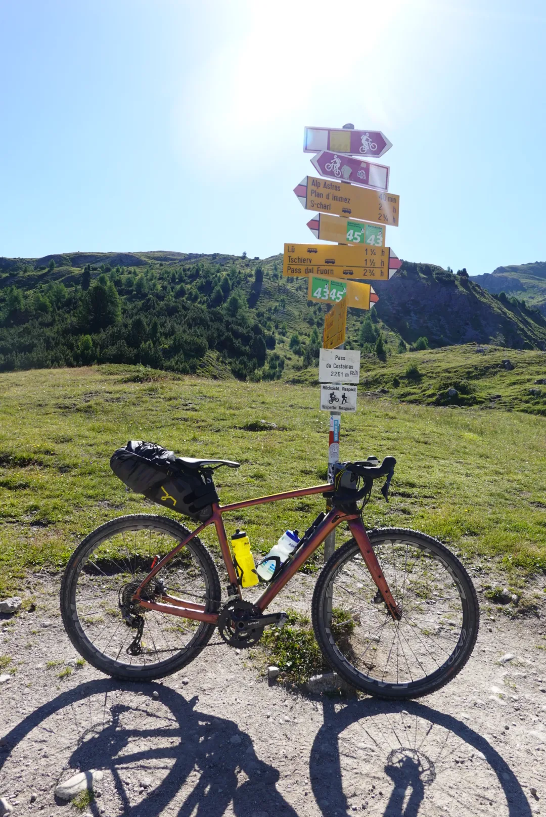Gravel bike below a signpost on an alpine meadow in the morning sun