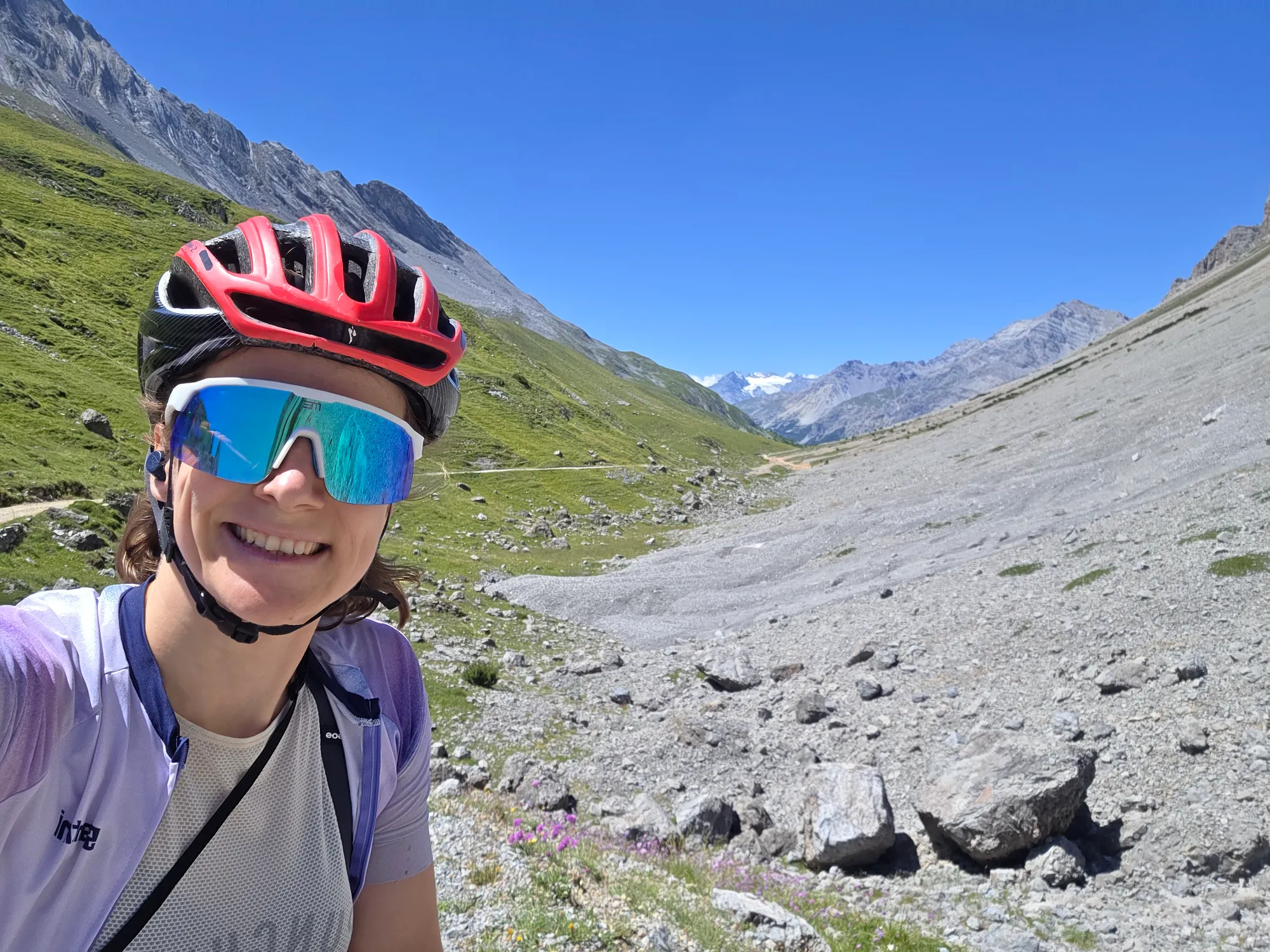 Carla in a red helmet and sunglasses in front of a scree slope