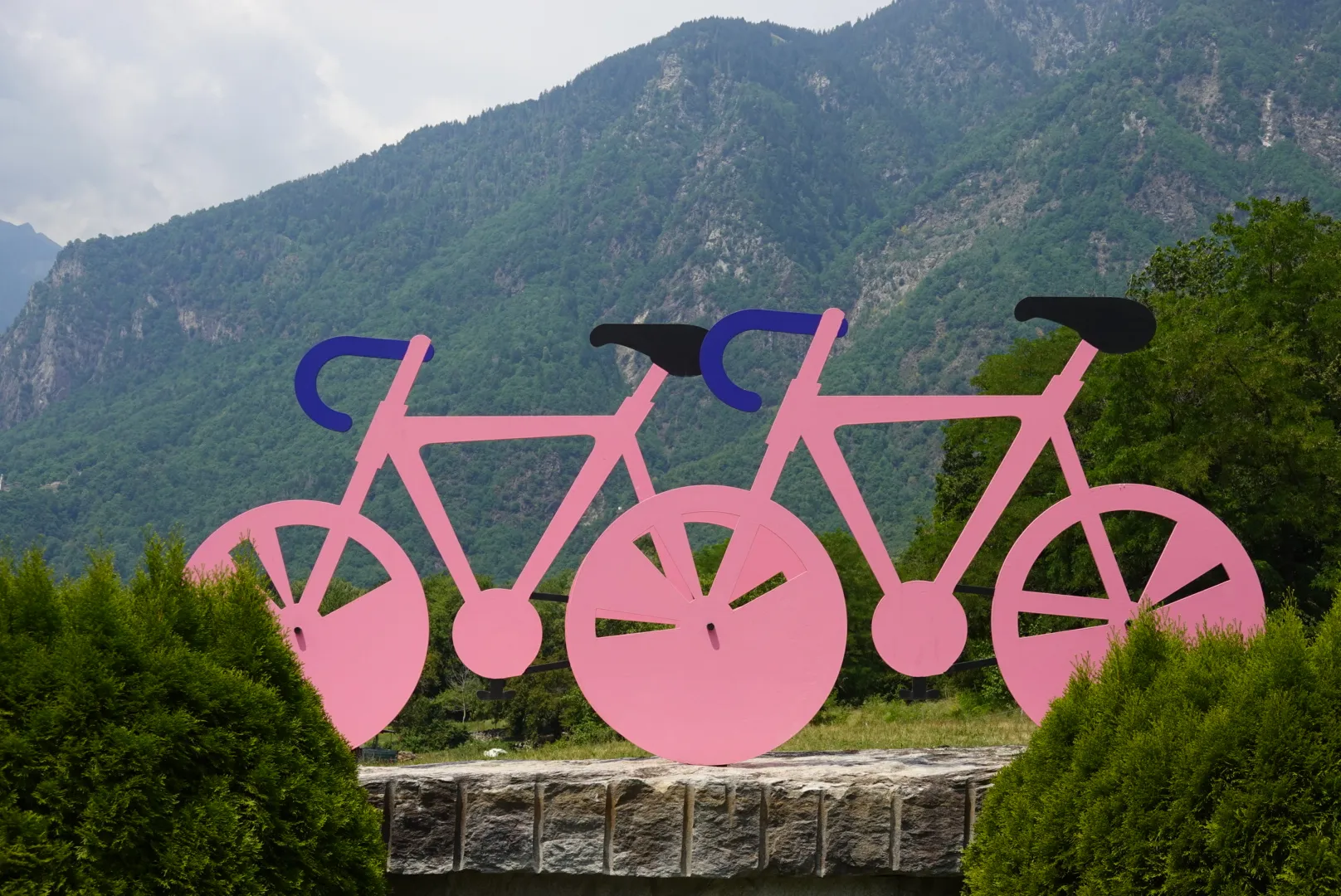 Two pink bicycle figures in front of green mountains