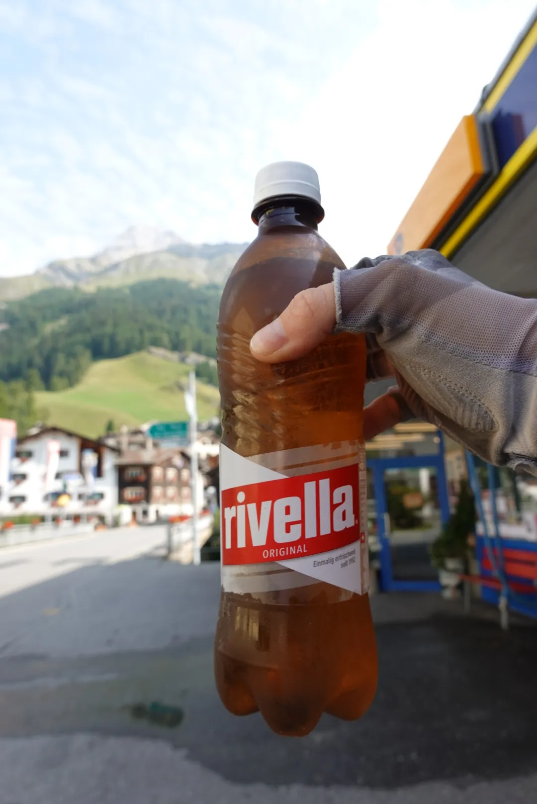 A bottle of Rivella in hand, a mountain village behind