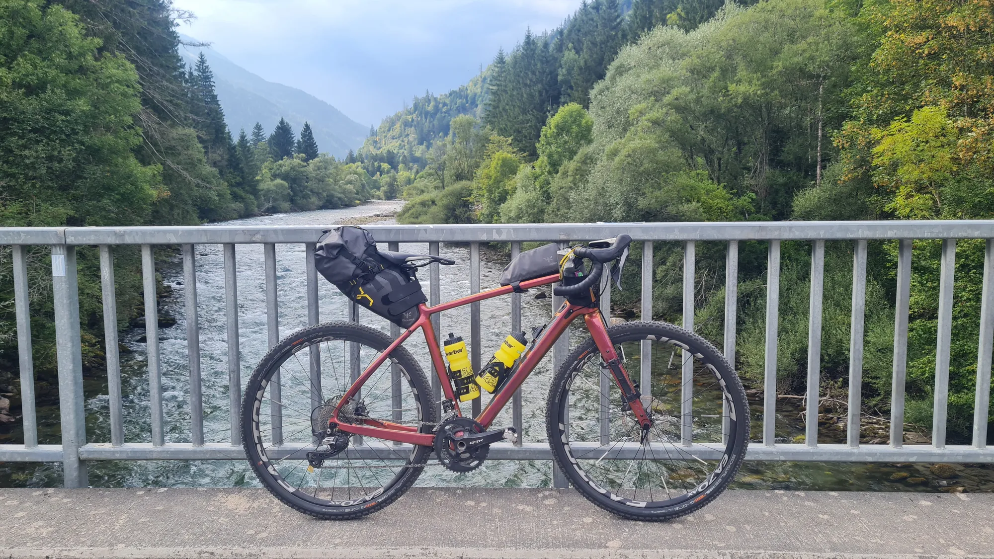Loaded bike against a bridge railing above a mountain stream