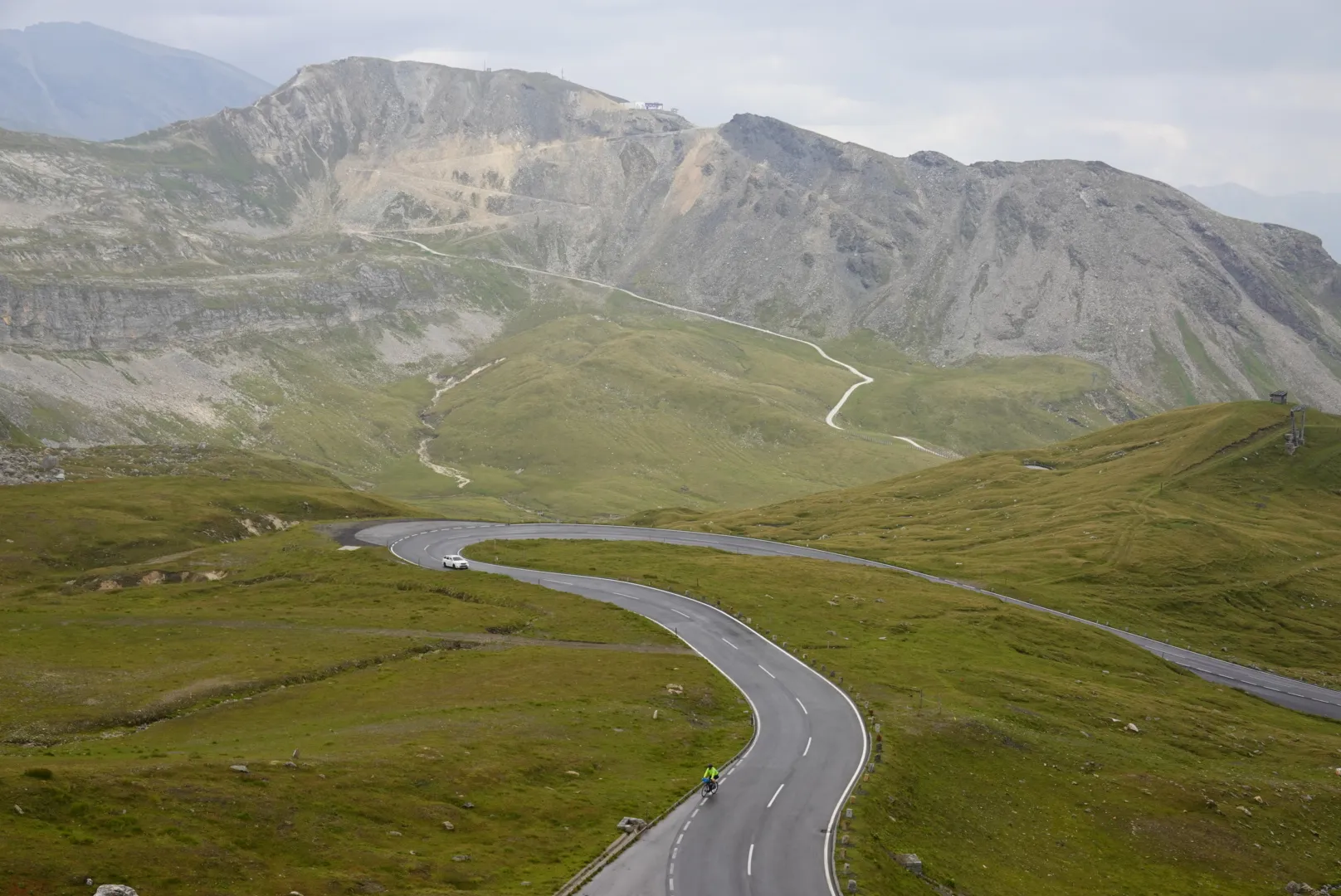 The road winding through alpine meadows below a grey ridge