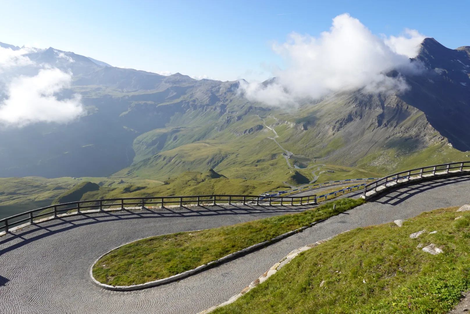 Cobbled hairpin with wooden railing, clouds over the peaks behind