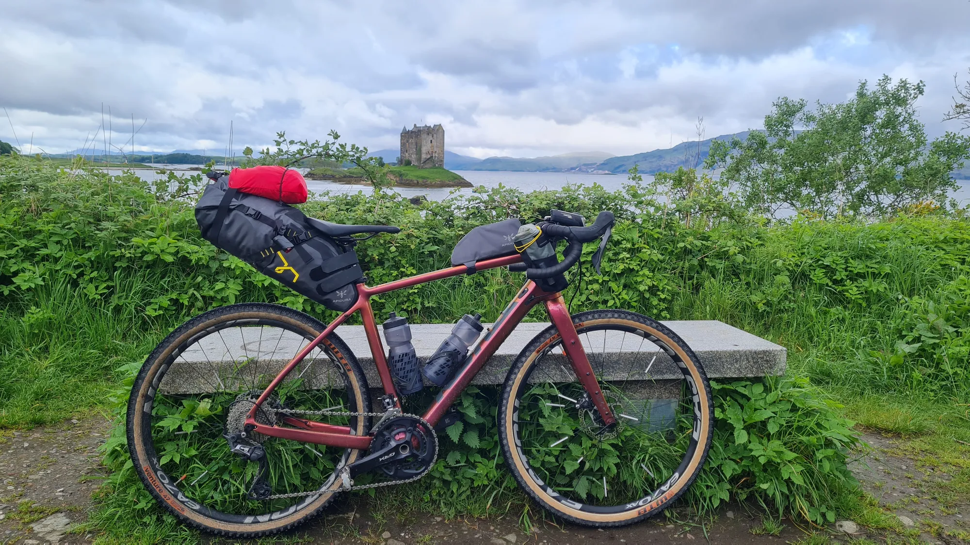 Loaded gravel bike against a bench, Castle Stalker in the background