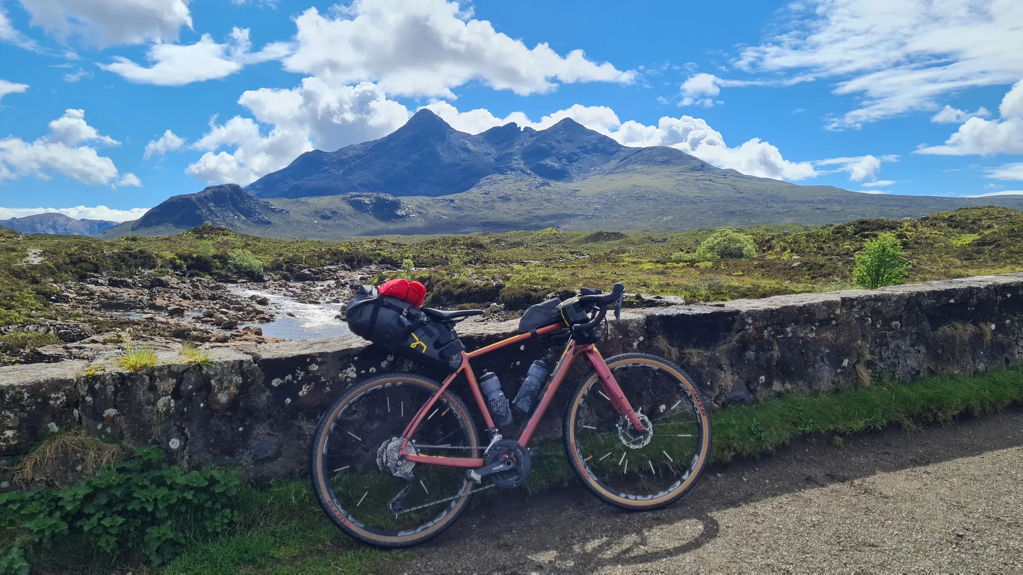 Loaded gravel bike against a stone wall in front of the Cuillin mountains on Skye