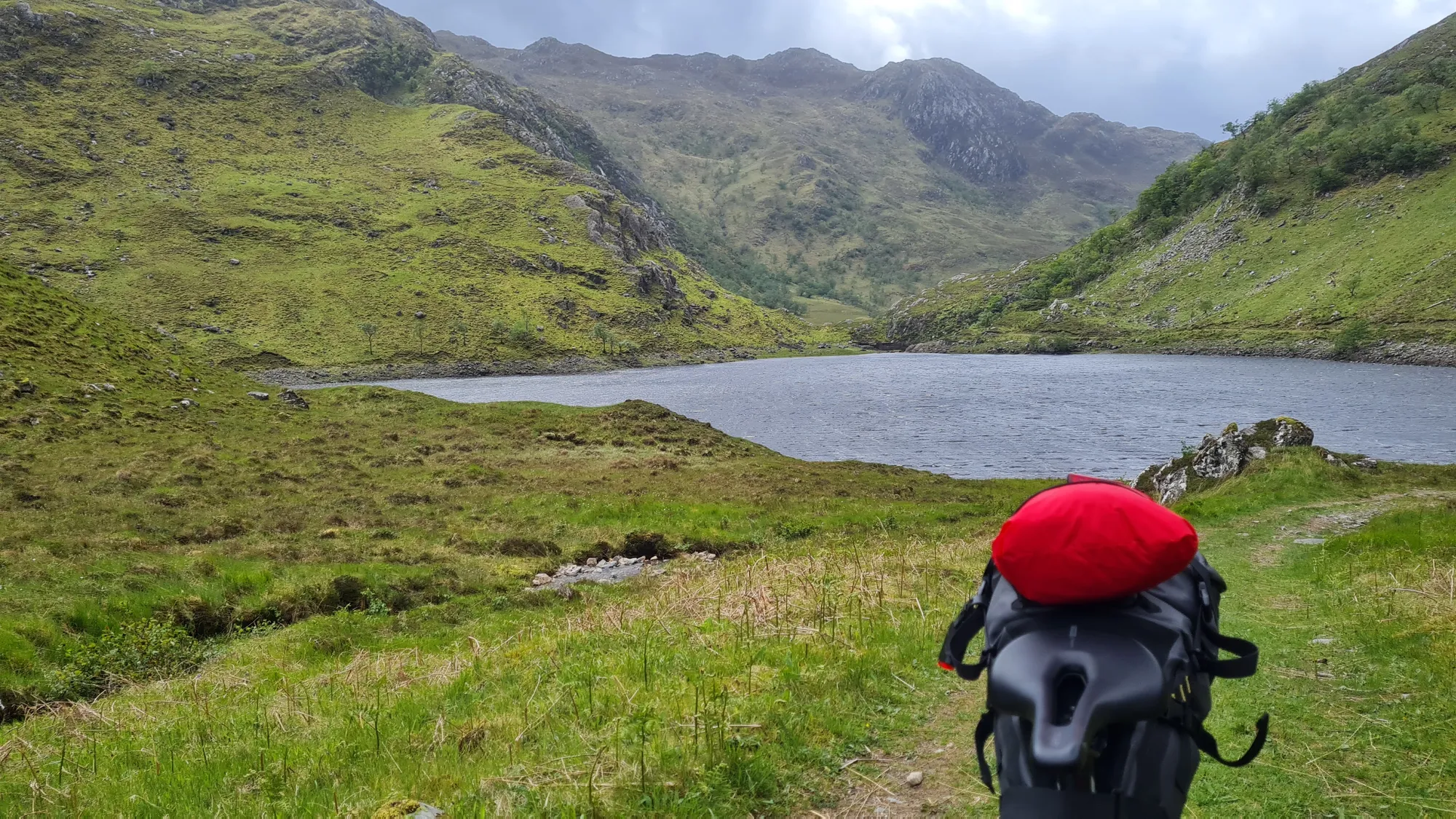 View over the handlebar bag to a loch between green mountains