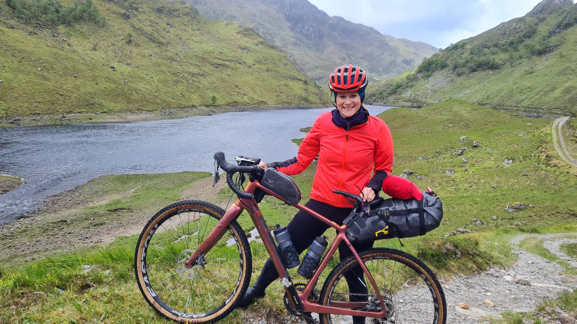 Carla with her bike above the loch, a gravel track winding into the valley