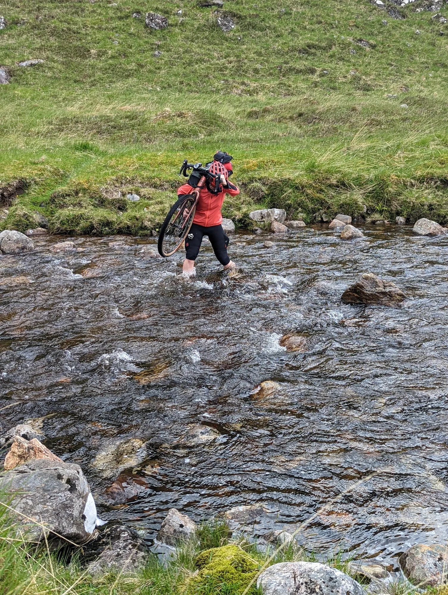 Carla carrying her bike through a rocky stream