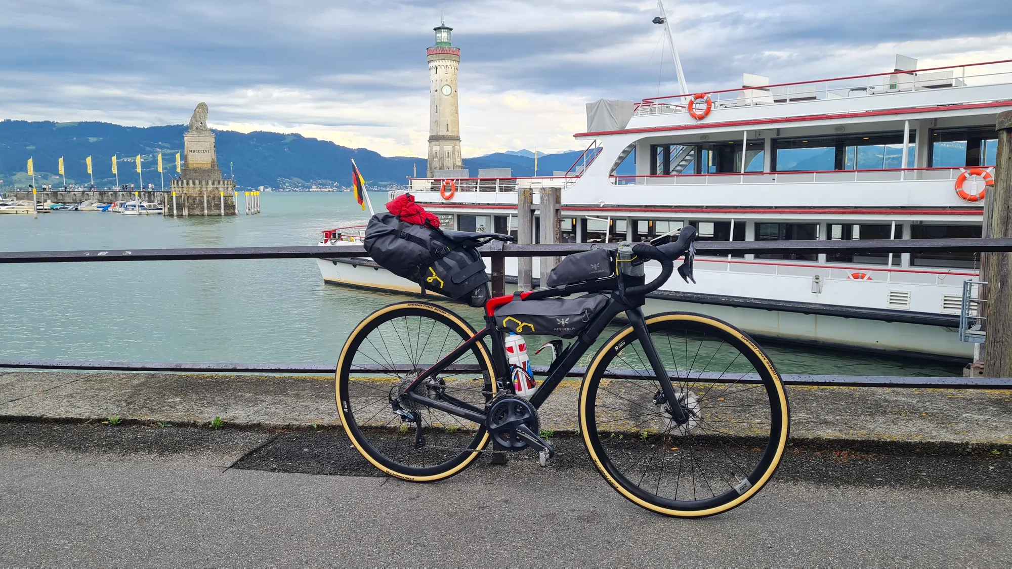 Loaded road bike at Lindau harbour, lighthouse and excursion boat behind