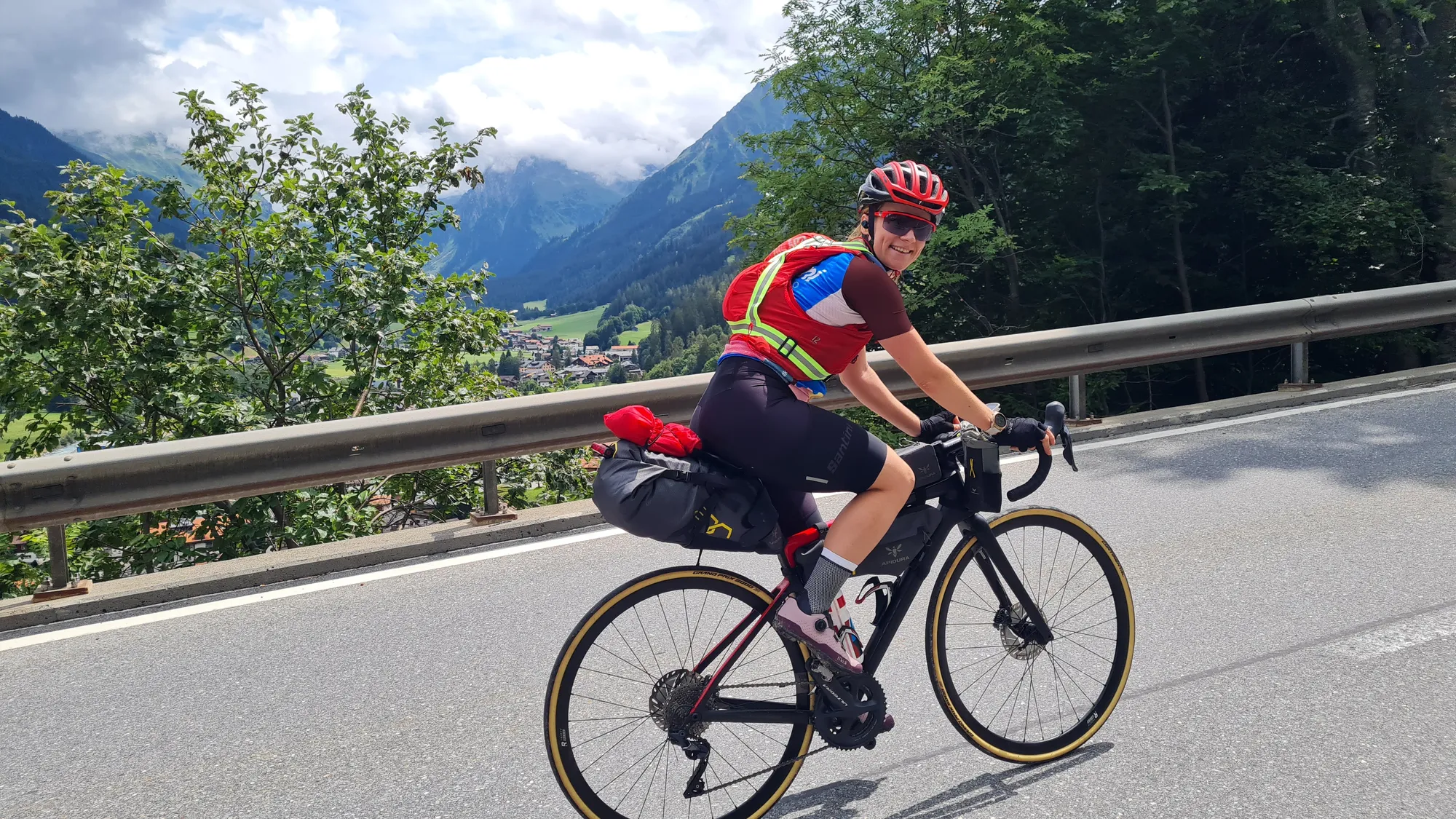 Me on the loaded road bike, a green valley with clouds behind me